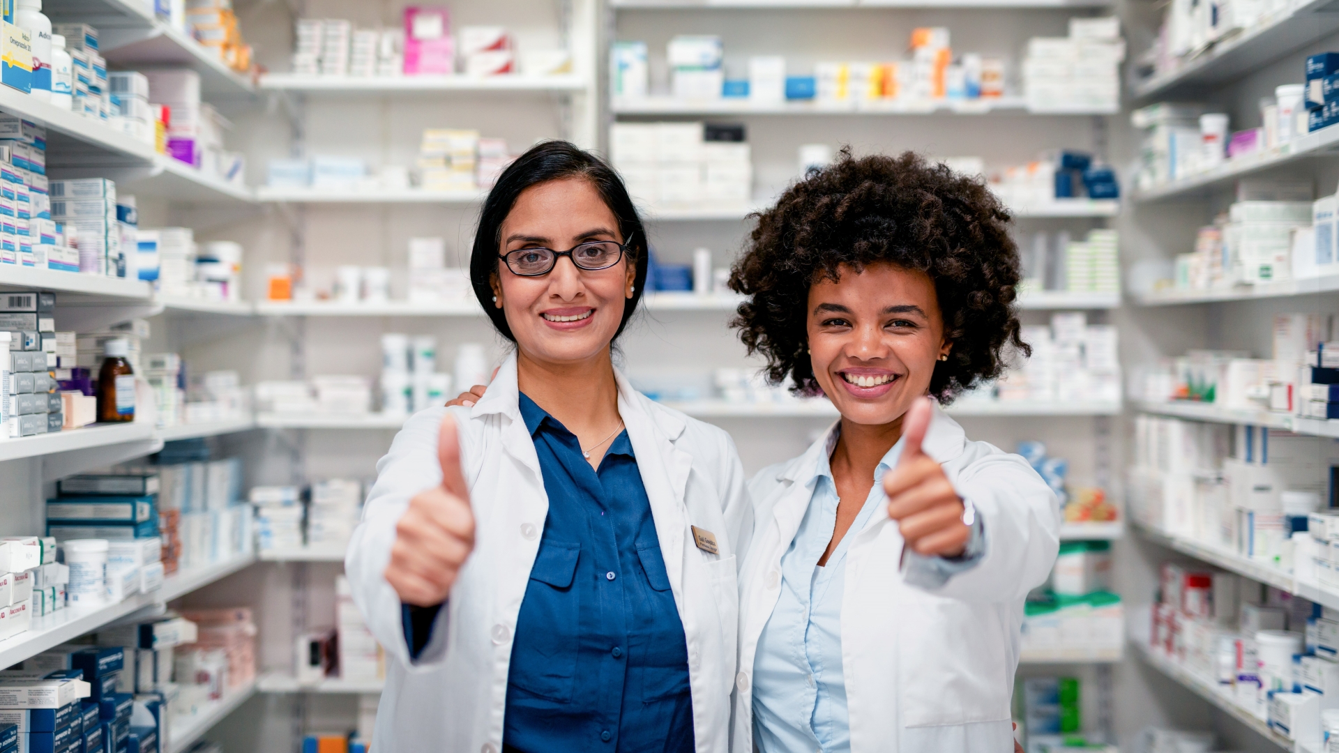 Two Professional Pharmacists Smiling and Giving Thumbs Up in a Pharmacy Setting.
