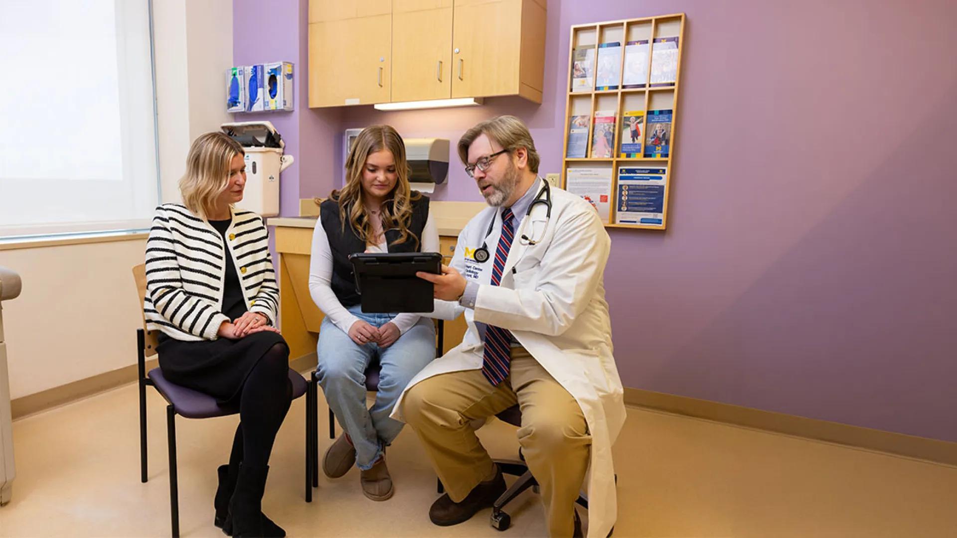A male doctor, a teenage girl, and a woman sit together and discuss paperwork in a medical setting