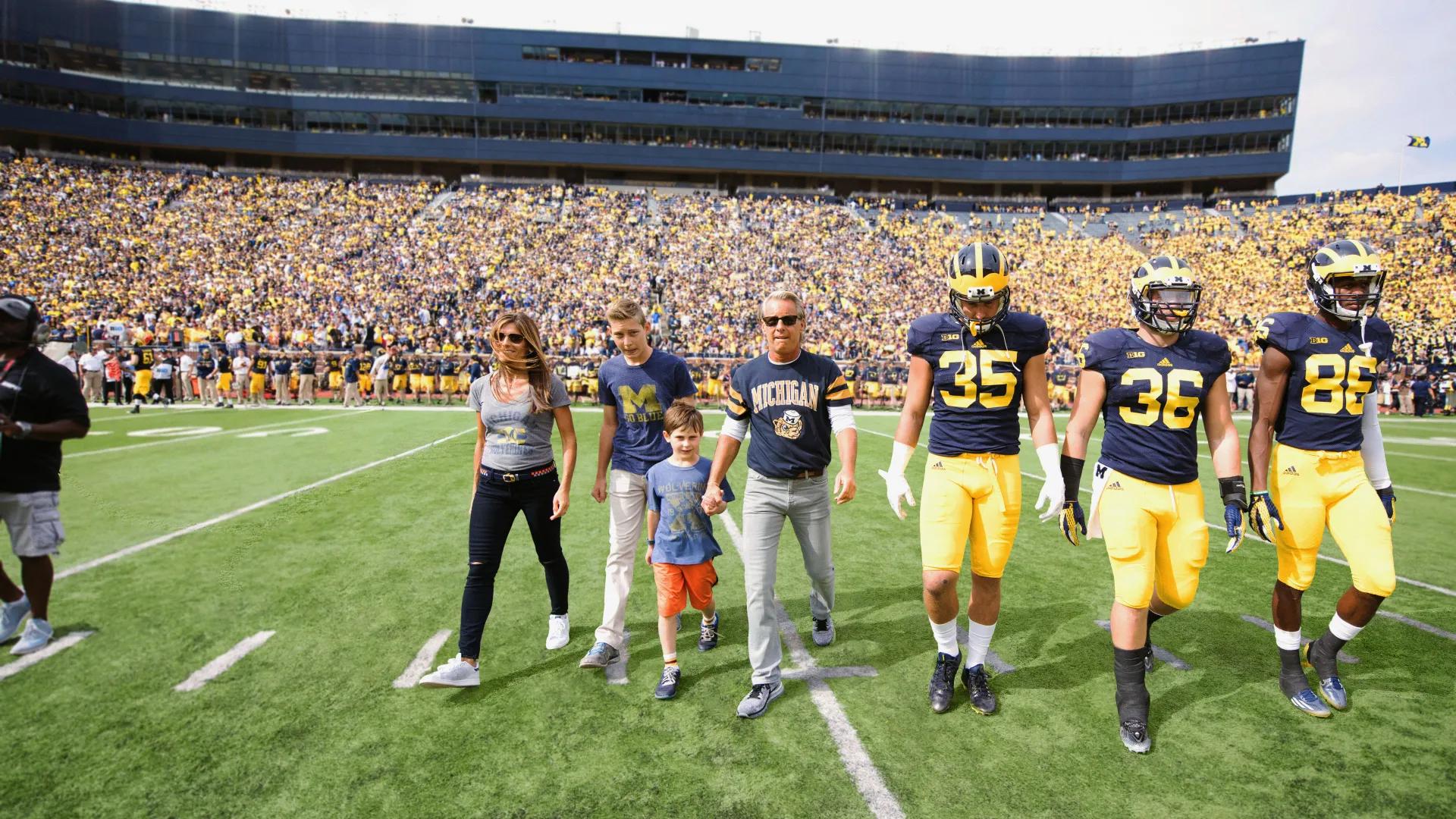 Forbes family walking on U-M football field with U-M football players alongside