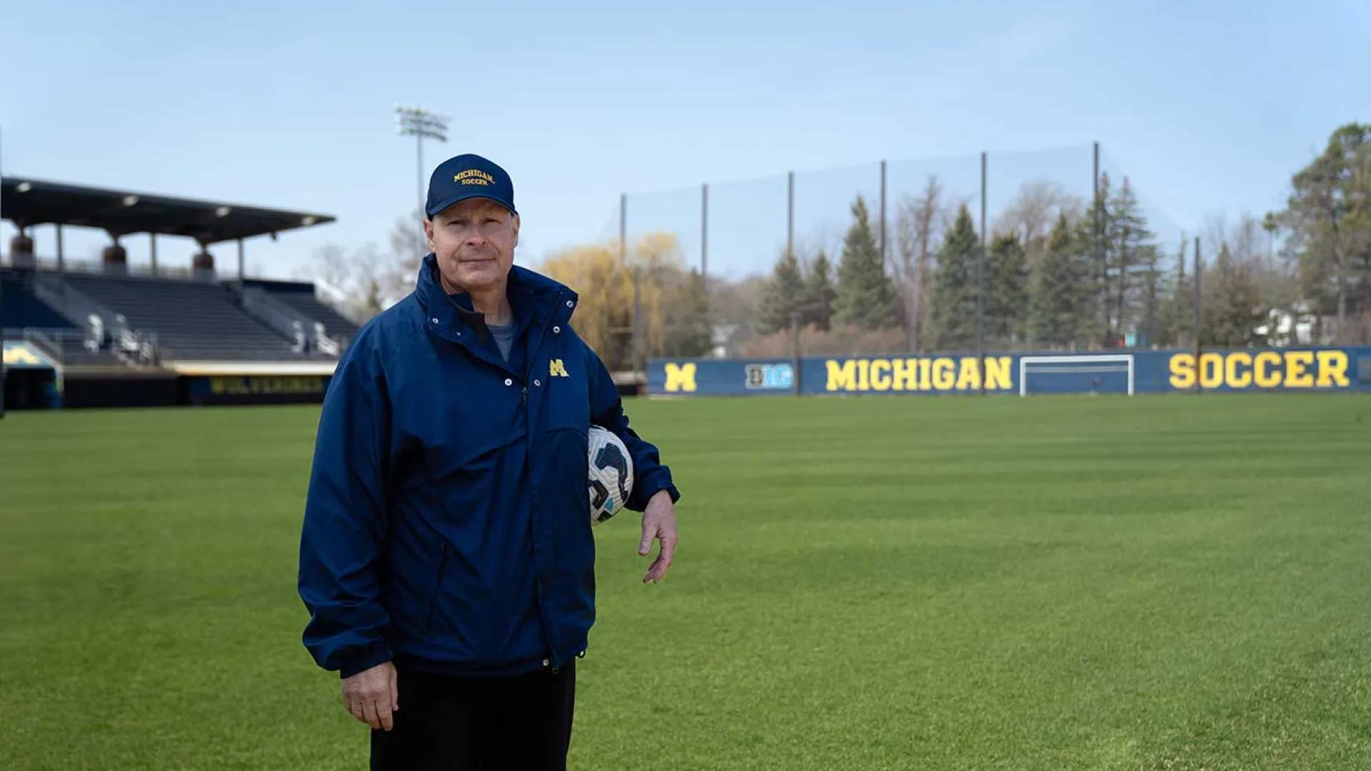 Steve Burns standing with a soccer ball under his arm on the University of Michigan practice field