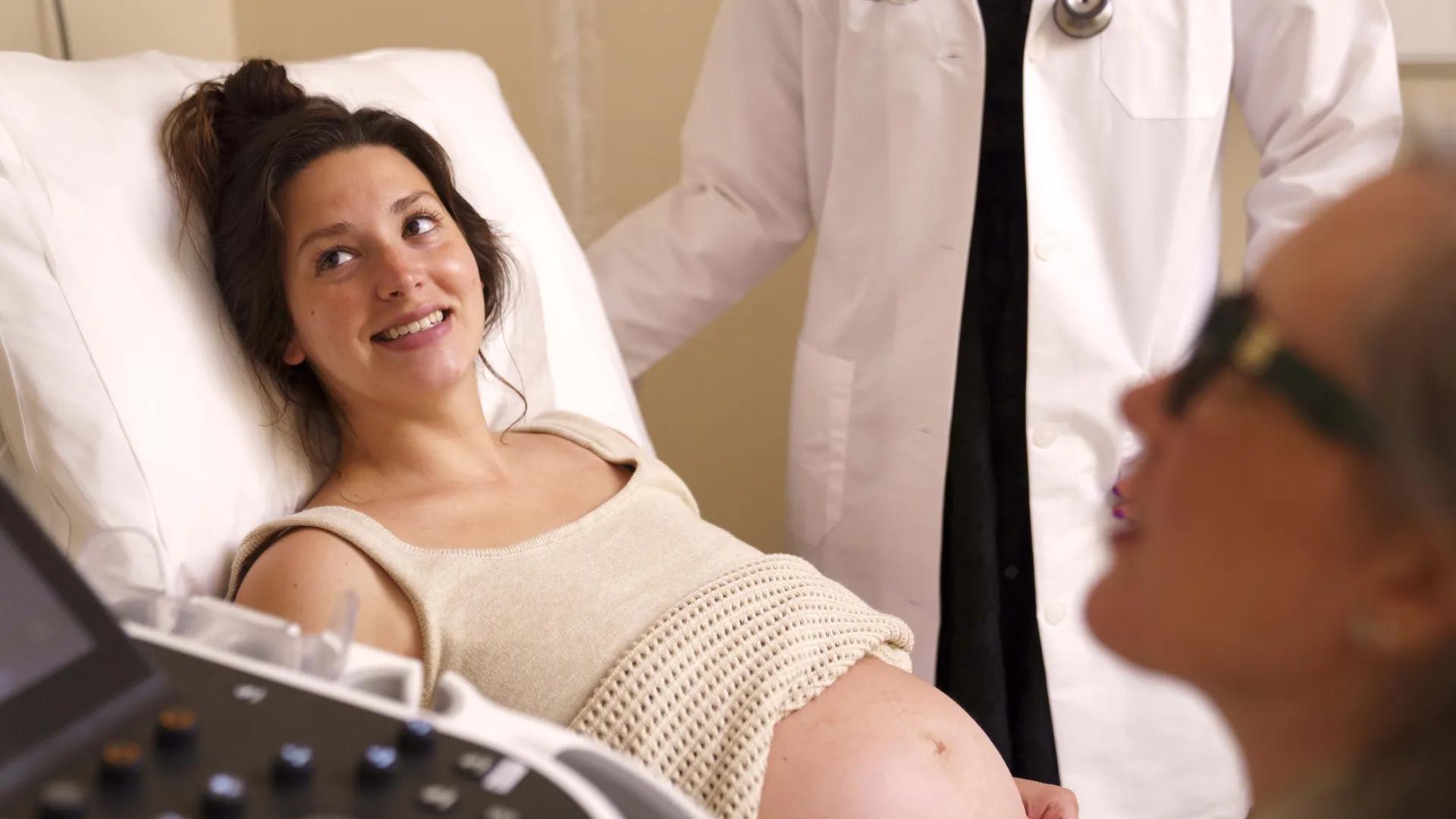 Pregnant woman on hospital bed looks up to provider, smiling