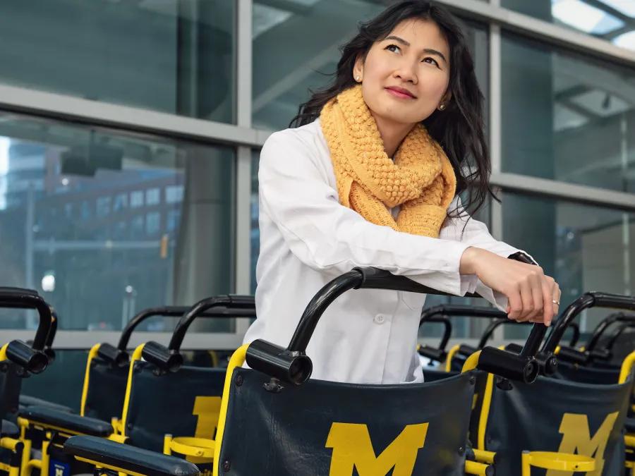 women in labcoat and scarf standing among a fleet of Michigan Medicine wheelchairs