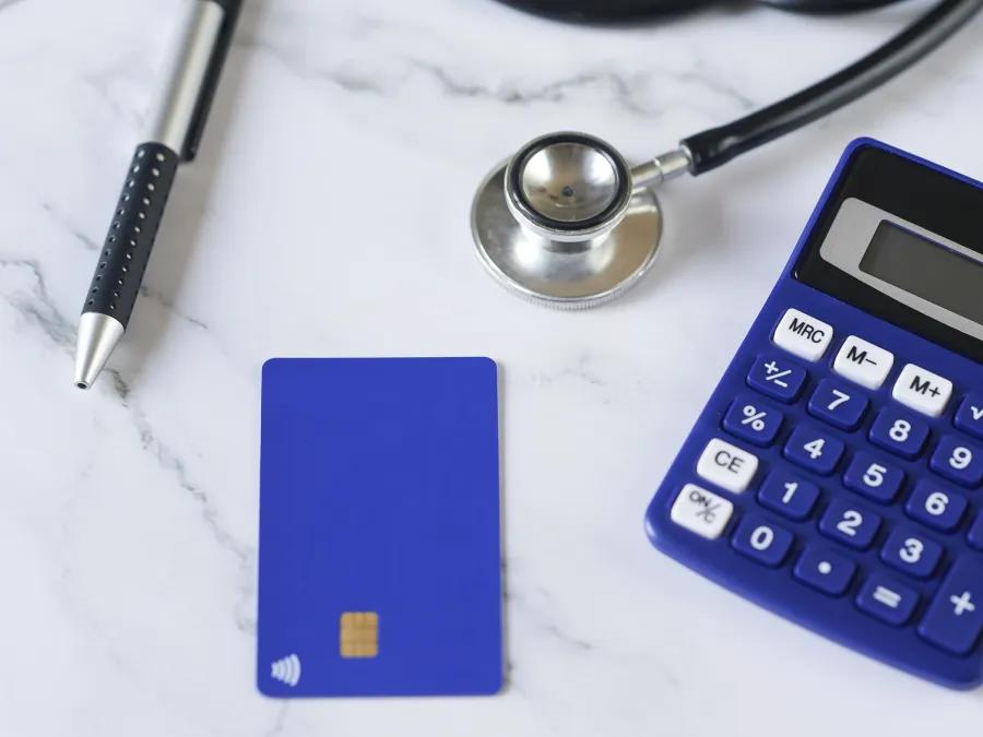 Calculator, stethoscope, blue credit card and pen lying on white marbled countertop