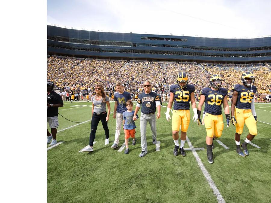 Two football players walk with the Forbes family on the U of M football field