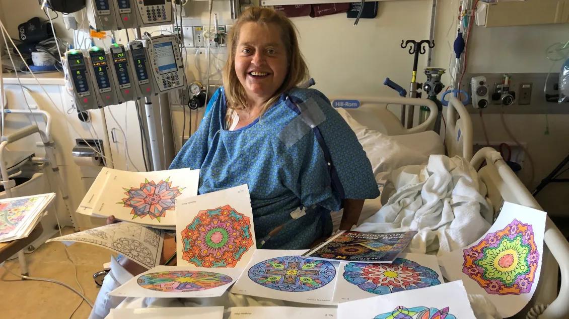 A patient sits with several completed coloring pages
