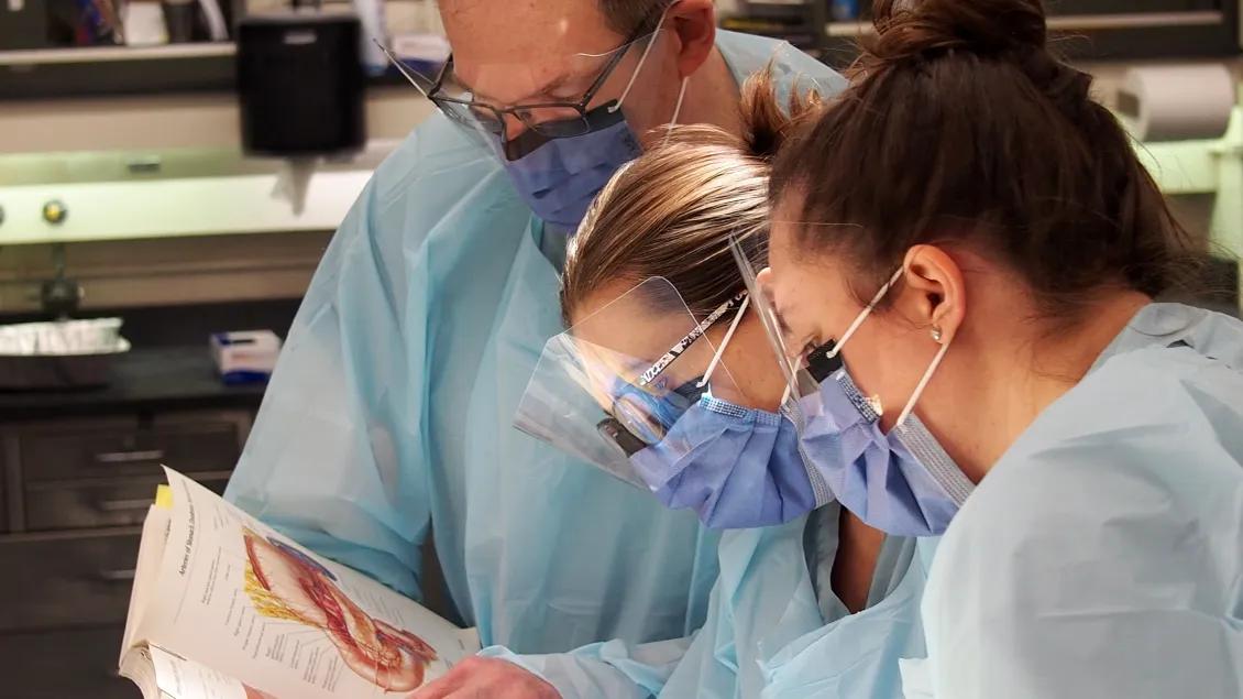 lab students and professor in gear reading textbook