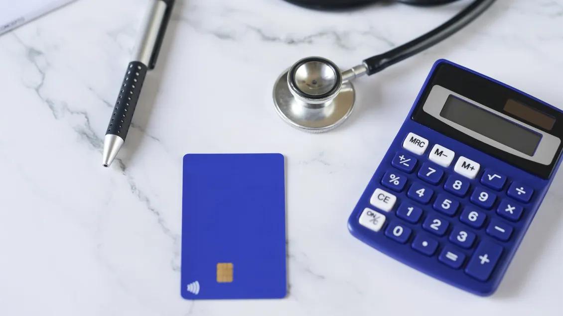 Calculator, stethoscope, blue credit card and pen lying on white marbled countertop