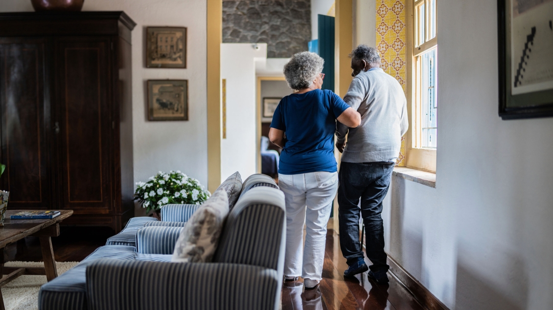 older woman walking with older man look from behind in their home