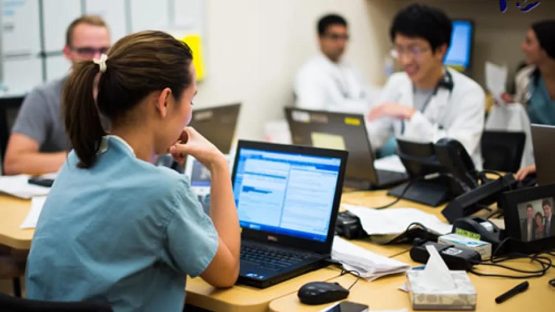 Trainee in front of a laptop at a table with other people in front of laptops.