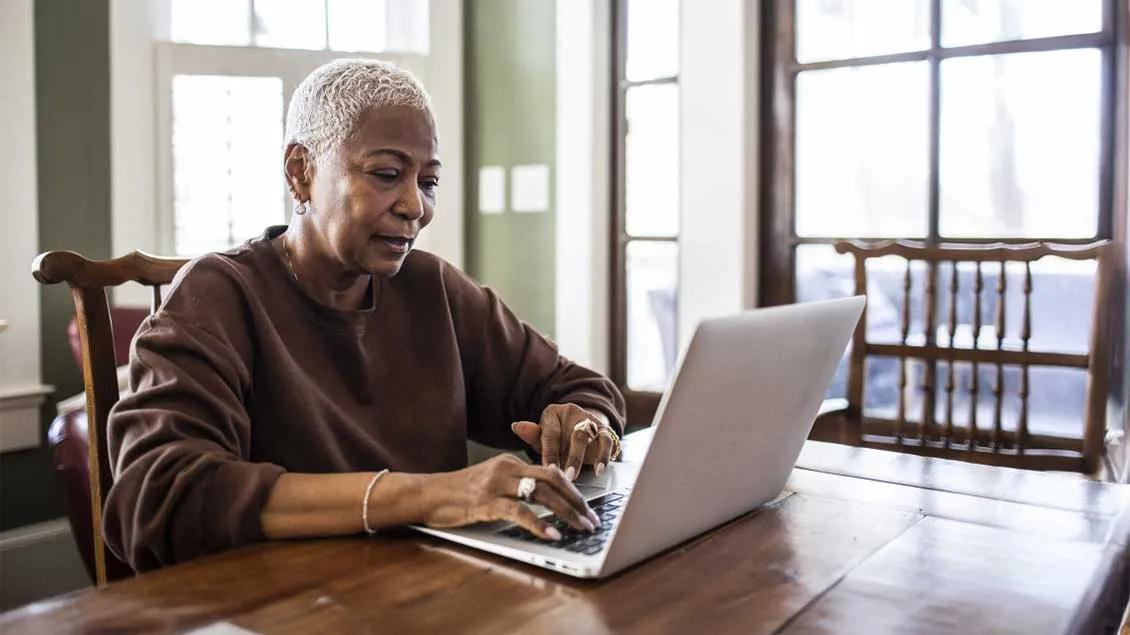 women is sitting at her kitchen table on a laptop computer