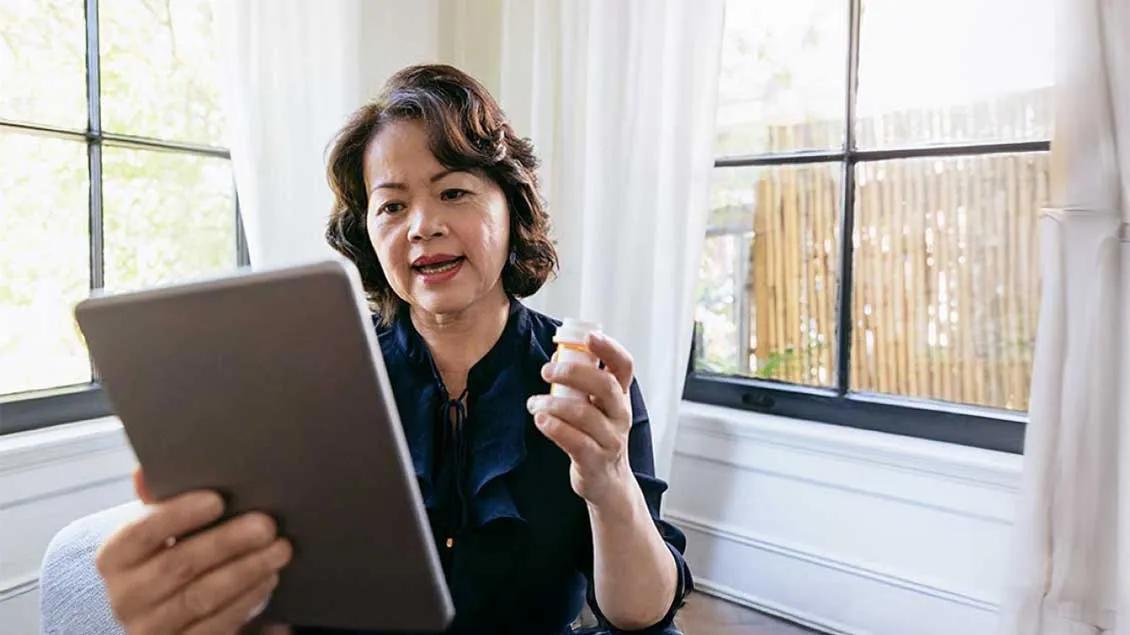woman is sitting in her chair while holding her tablet and prescription bottle