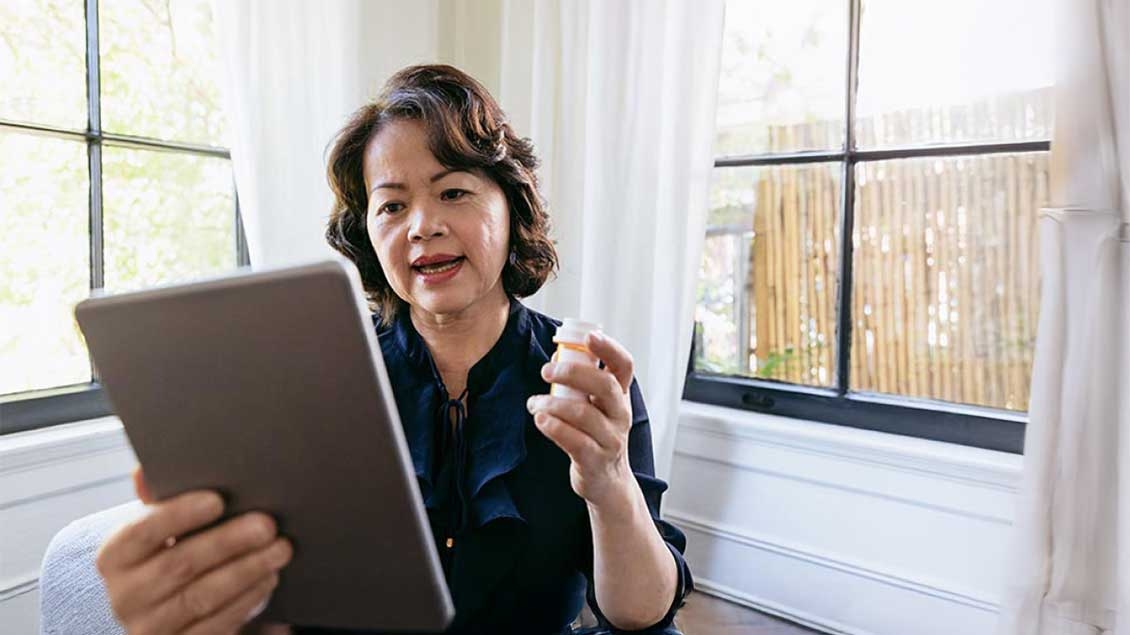woman is sitting in her chair while holding her tablet and prescription bottle