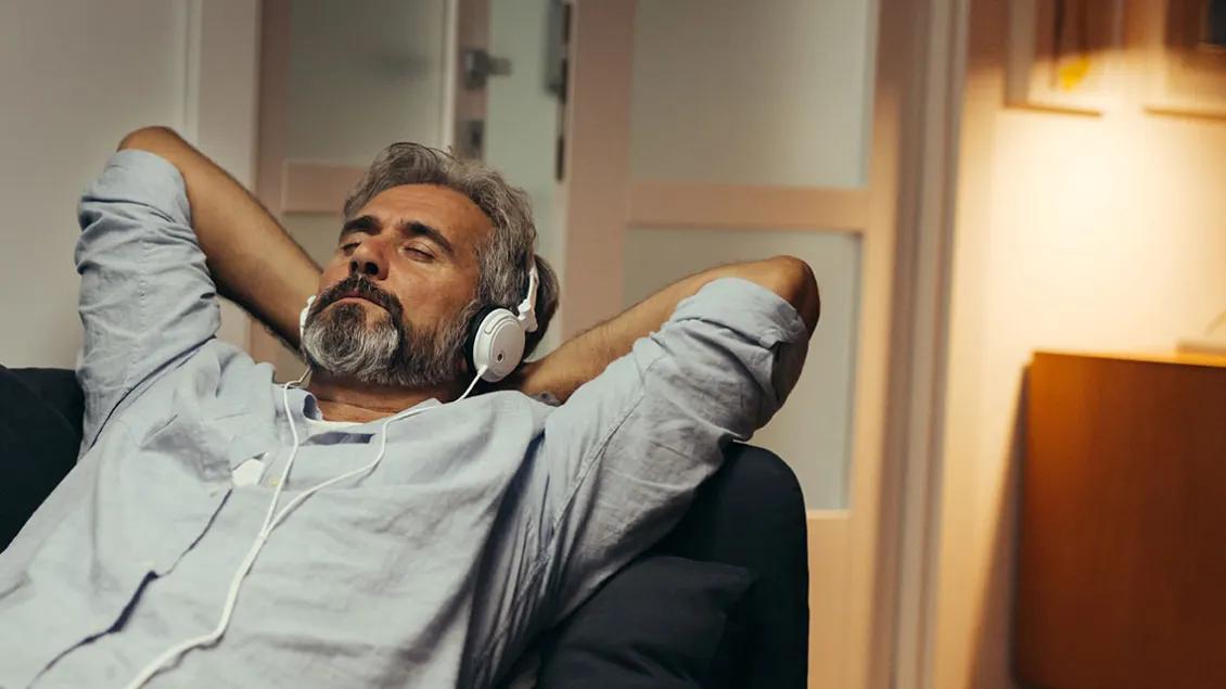 Mature bearded man leans back as he listens with his headphones