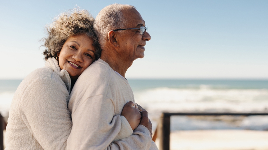 Couple in white sweaters and graying hair on the beach.