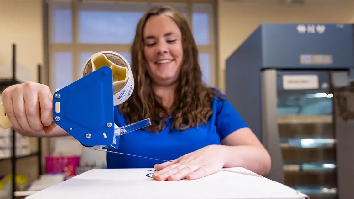 Person holding a blue packing tape dispenser while sealing a box.