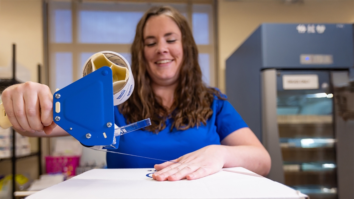 Person holding a blue packing tape dispenser while sealing a box.
