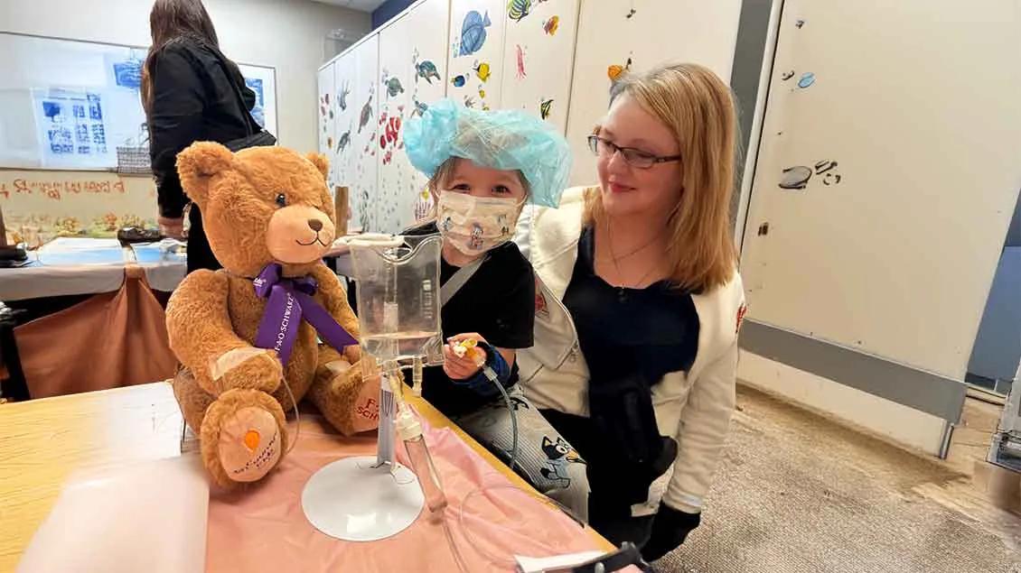A little girl and a woman sit together with a teddy bear