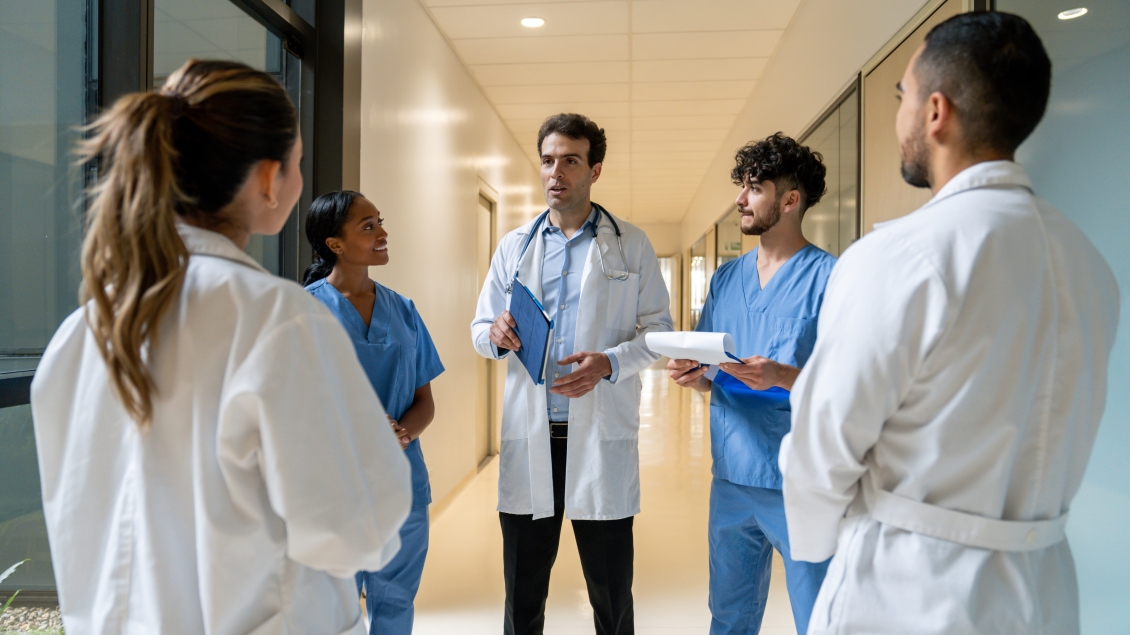 Healthcare professionals in lab coats and scrubs discussing patient care in a hospital hallway.