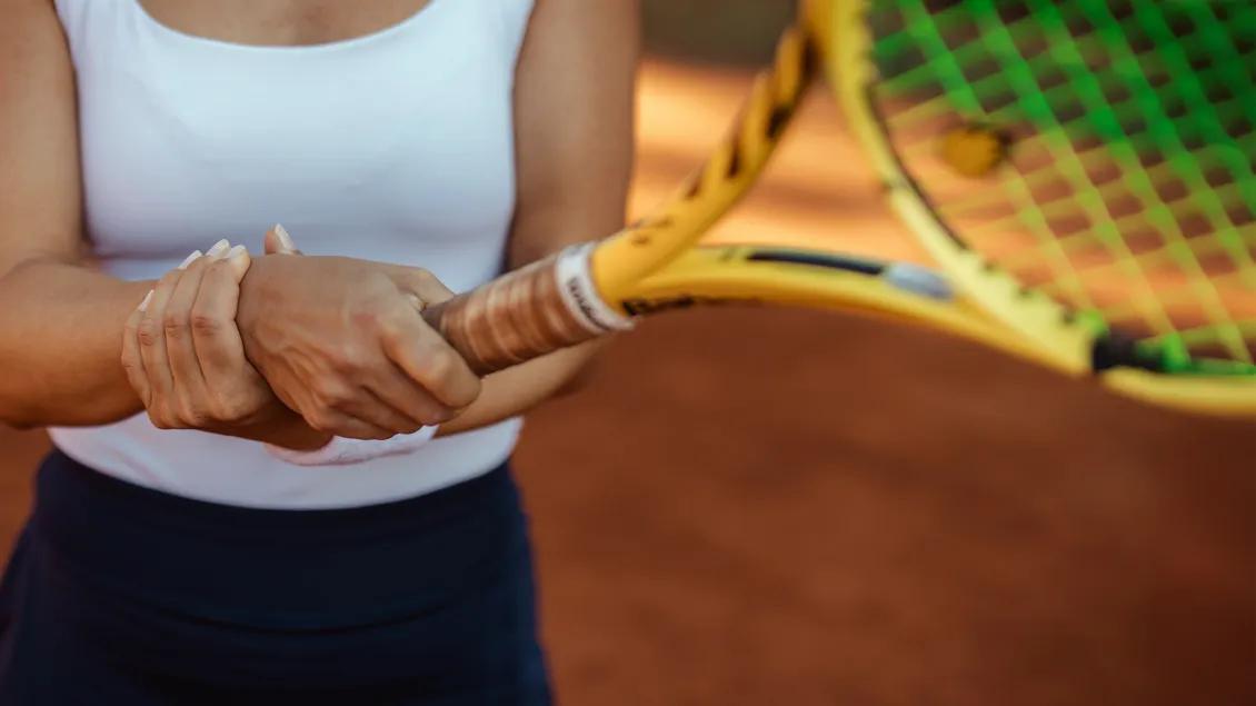 Torso of woman holding her wrist with one hand and a tennis racquet with the other