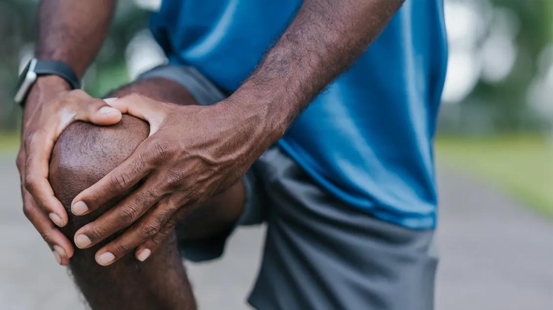 Black man wearing a sport watch and shorts holding his knee with both hands