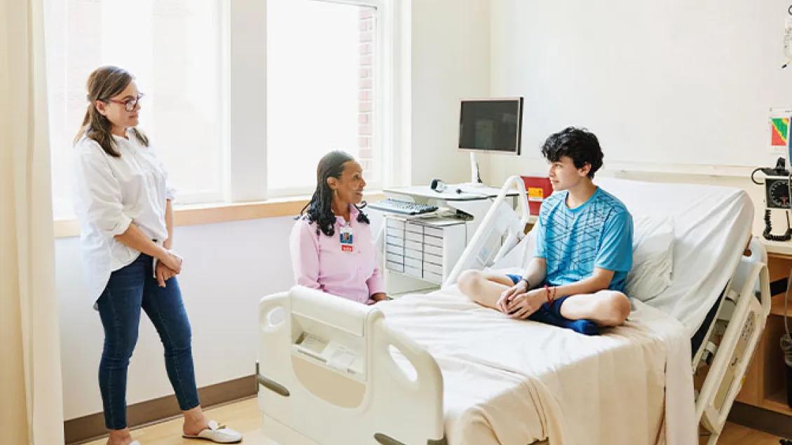 teen boy sits in hospital bed speaking with two female health providers