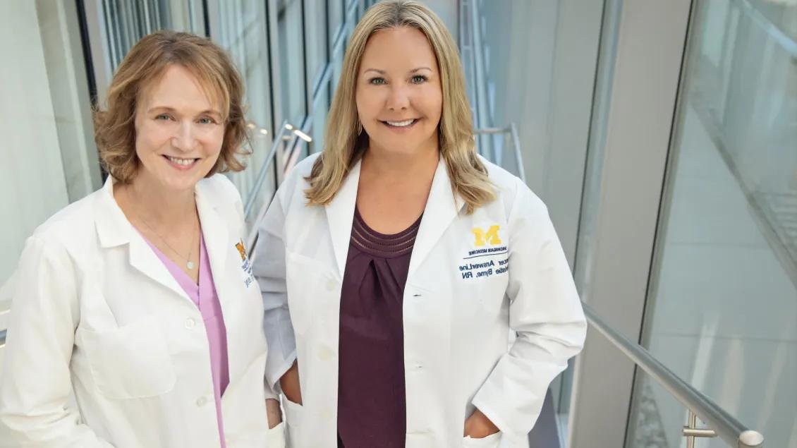 Two Cancer Answer Line call representatives in white coats standing on a stairway surrounded by windows