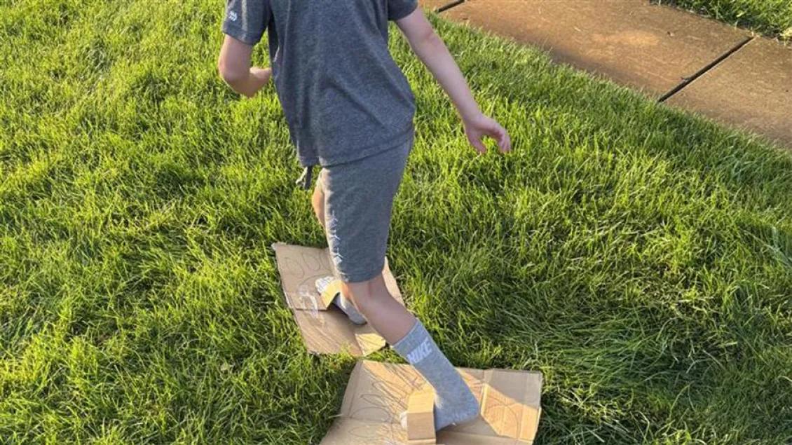 Child racing while wearing big feet made out of cardboard with taped on loops for their feet.
