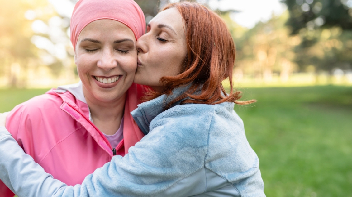 Two women embracing, one in pink and one in blue. The one in pink has on a headscarf.