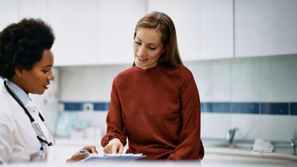 Provider with a patient in an orange sweater and long brown hair looking at a chart in an exam room.
