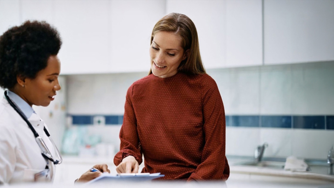 Provider with a patient in an orange sweater and long brown hair looking at a chart in an exam room.