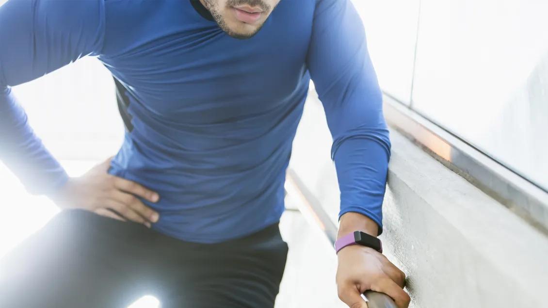Torso of man wearing blue shirt holding hip with one hand and railing with another