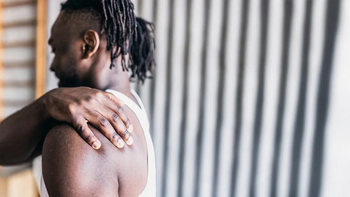 Black man with braids wearing white tank holding shoulder 