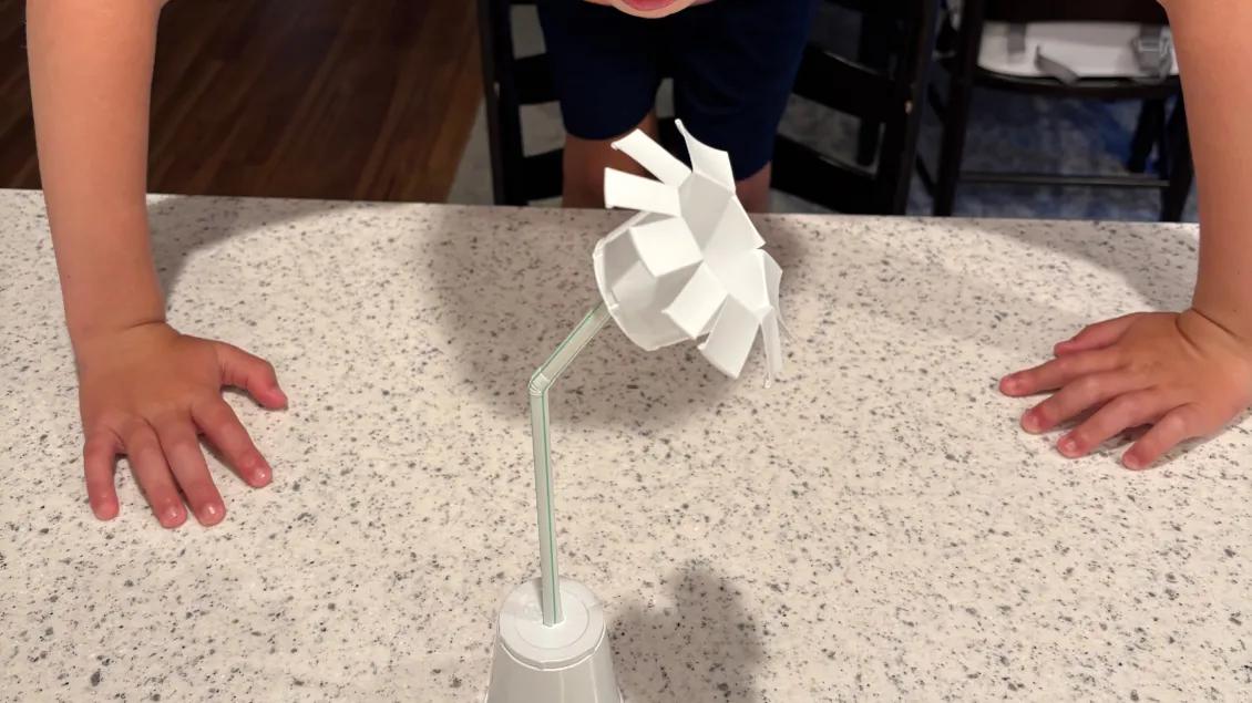 boy blowing on paper cup windmill to power it
