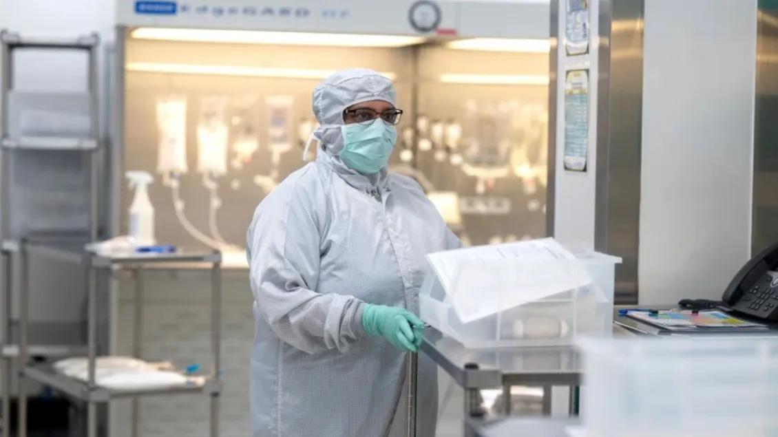 A healthcare worker in protective gown, mask, gloves, and hair covering working in a sterile laboratory environment.