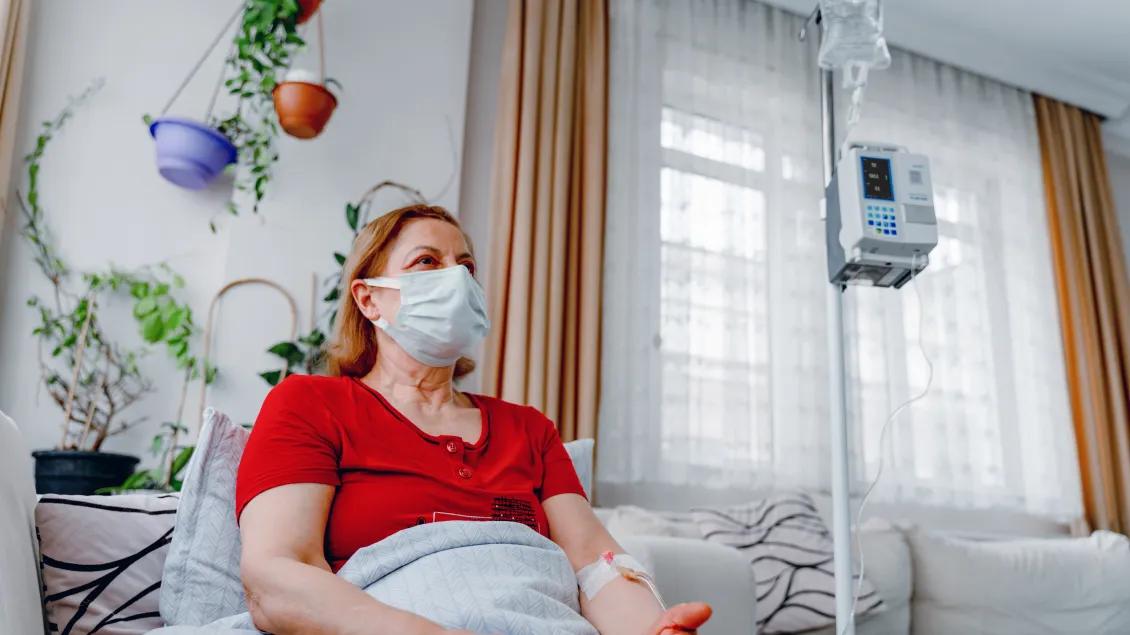 Woman in a red shirt and face mask sitting on a hospital bed.