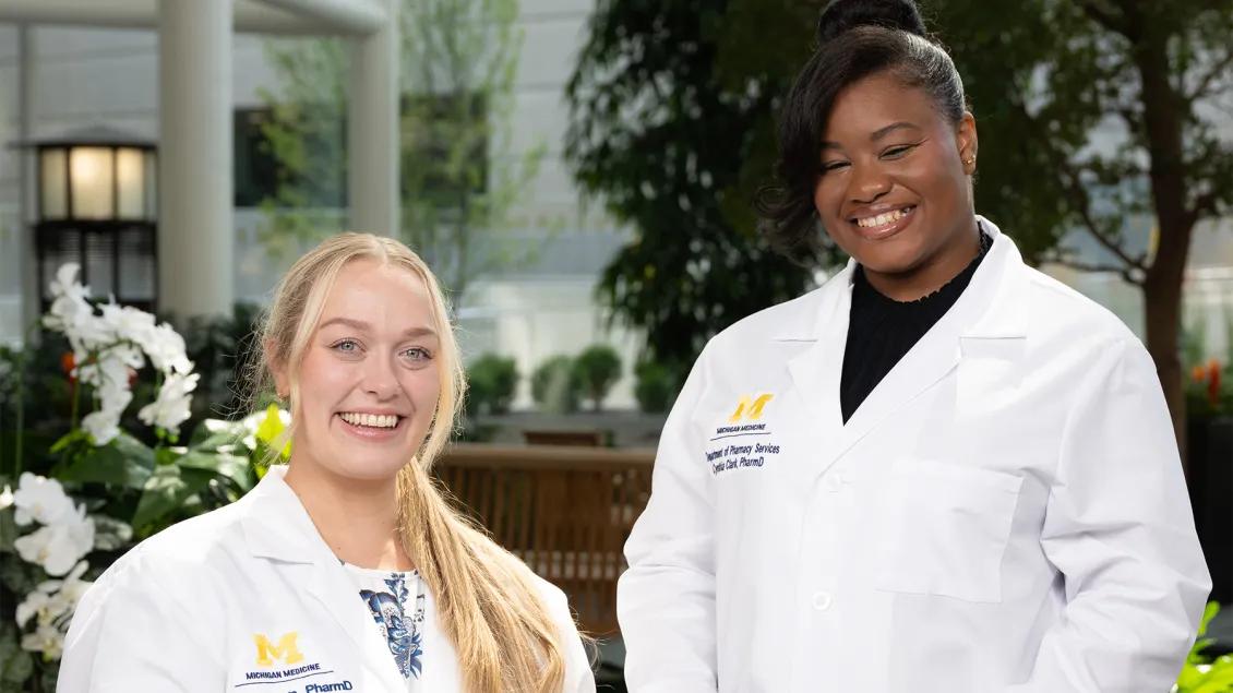 Two women wearing white pharmacy coats smiling