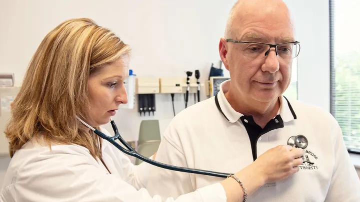 White female doctor uses a stethoscope to listen to an older white man's heart