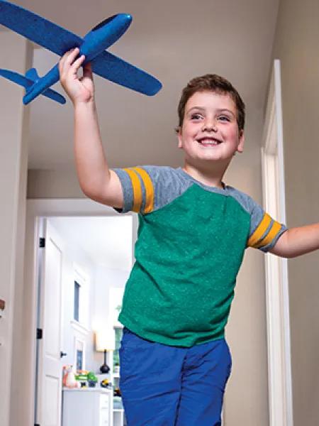 Little boy in green shirt and blue pants holding a blue toy airplane