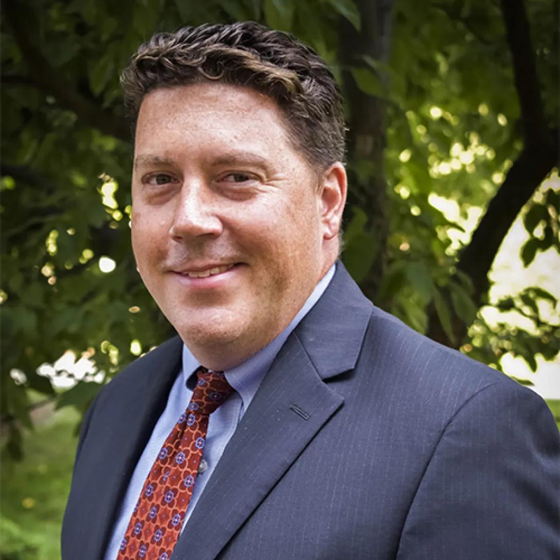 John Clark, headshot of white man with brown hair wearing navy blue jacket and red tiel