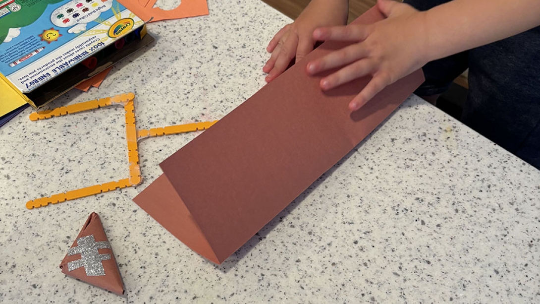 child folds brown paper to make paper football