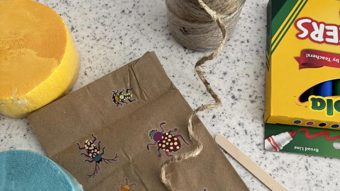 small paper bag with string, stickers and markers nearby