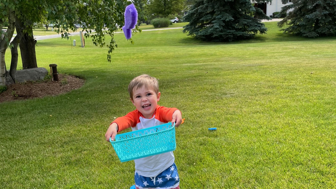 Child holding blue basket smiling in yard
