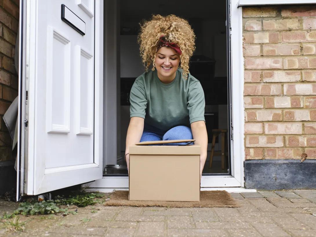  Happy young woman picking up packages from doorway.