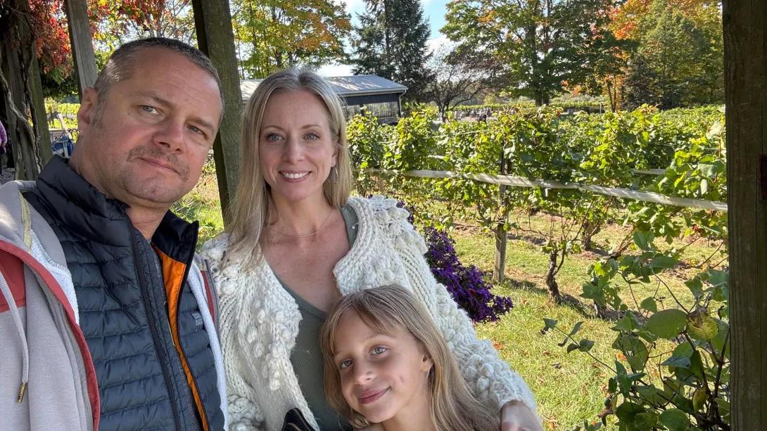 Man, woman and young girl pose at an apple orchard.